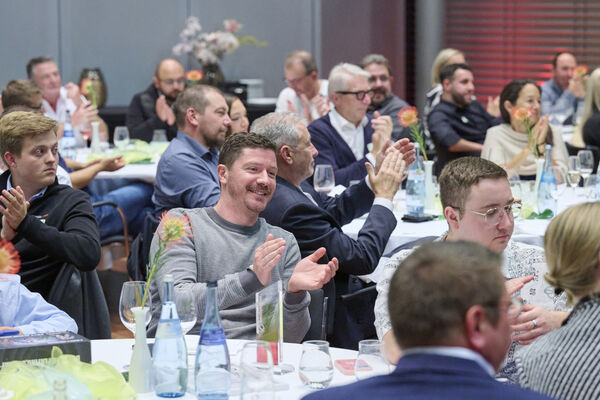Personen sitzen im Raum an runden Tischen zusammen und reden.