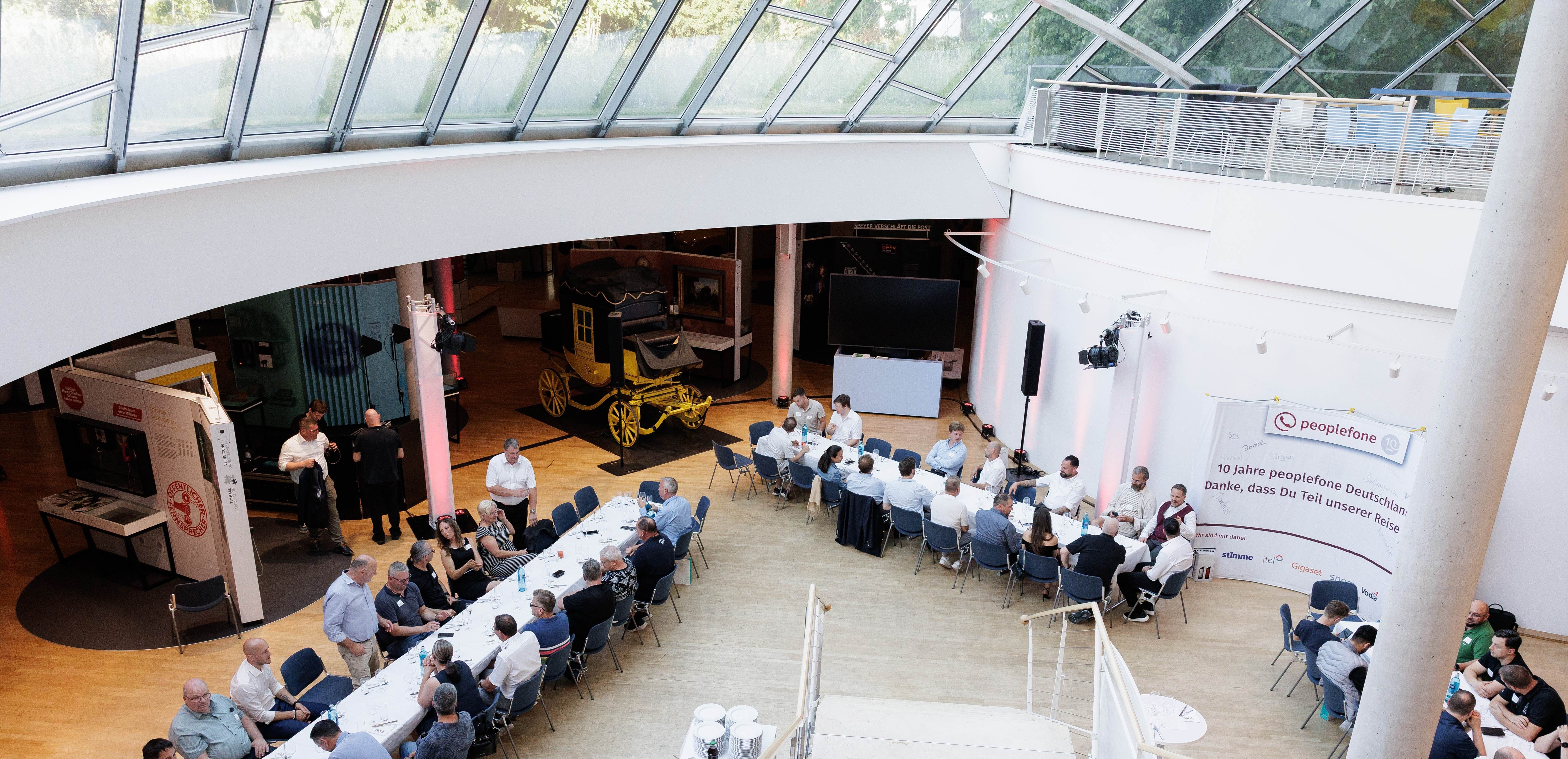 Blick in den Lichthof mit Messewand, gedeckten Tischen und Personen an den Tischen.