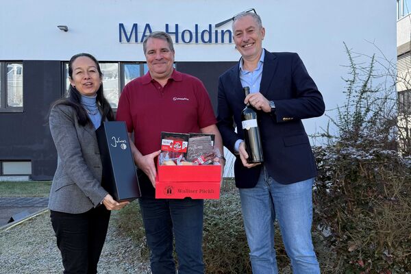 Personen vor einem Firmengebäude halten einen Präsentkorb in der Hand.