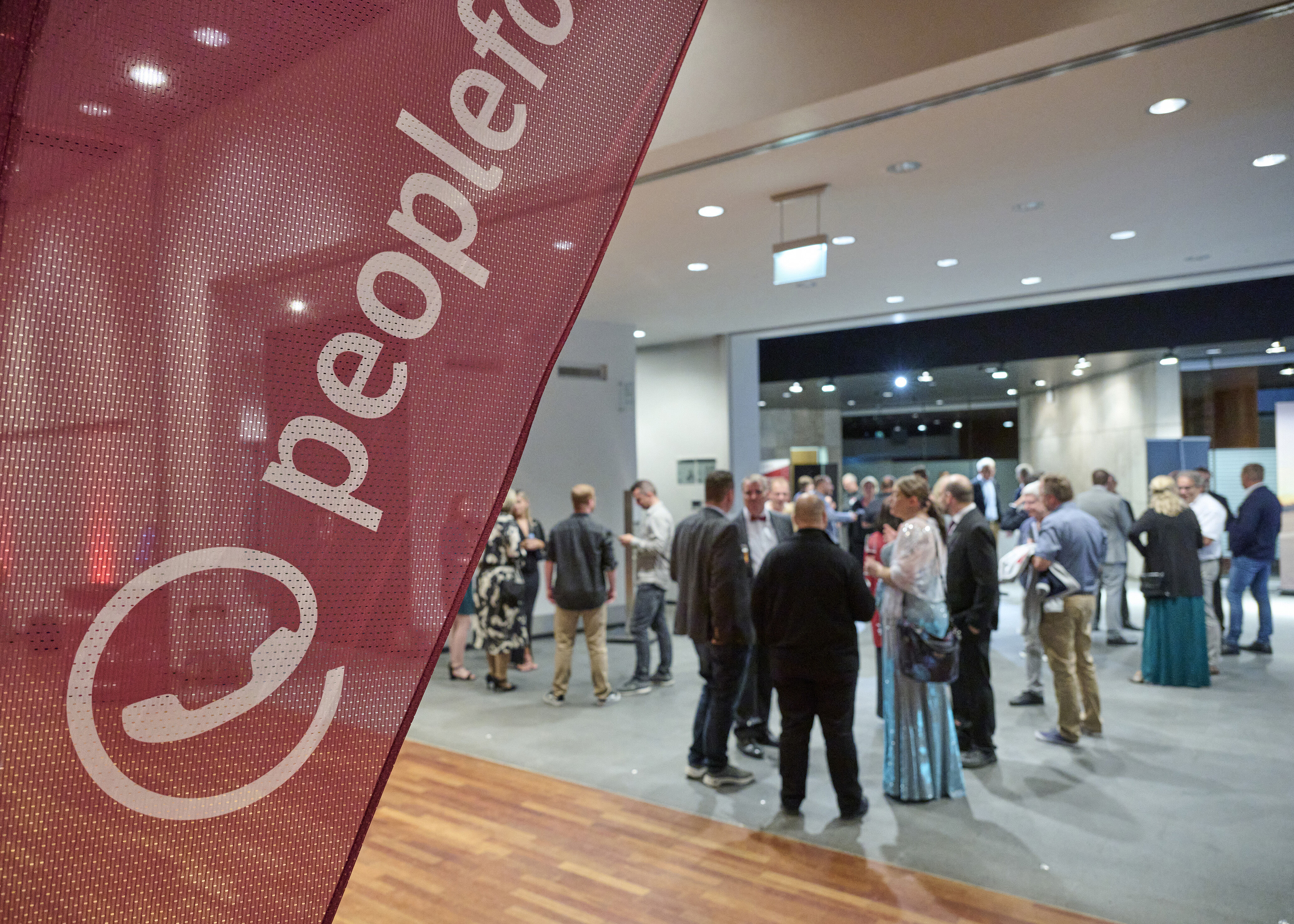 Blick in ein Foyer mit mehreren Menschen. Im Vordergrund eine Beachflag der peoplefone.