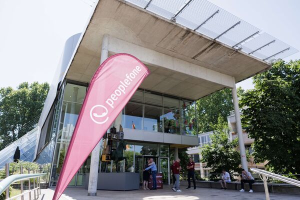 Gläserner Eingangsbereich des Museums. Im Vordergrund steht eine peoplefone Beachflag.