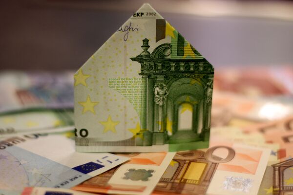Zu einem Haus gefalteter Geldschein steht auf weiteren Banknoten.
