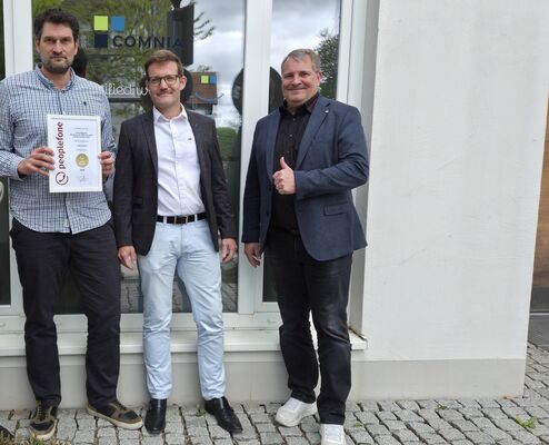 Drei Personen bei Comnia bei einer Urkundenübergabe.