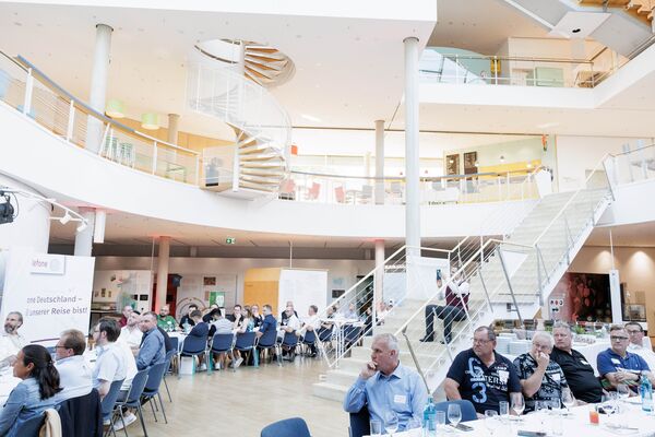 Mehrere Personen sitzen an Tischen im Lichthof, essen und unterhalten sich. Teile der Ausstellung sind im Hintergrund sichtbar.