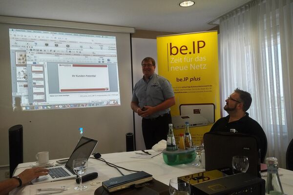 peoplefone Partner hören, an einem Tisch sitzend, dem Referenten zu, der an einer Leinwand steht.