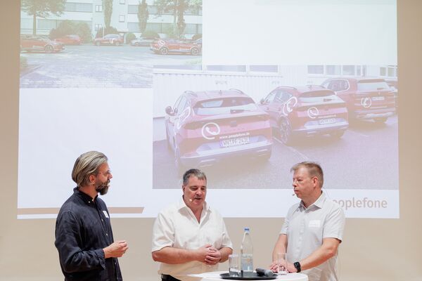 Drei Personen stehen vor einer Leinwand mit Headset und führen ein Gespräch.