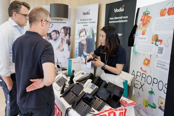 Ausschnitt von Personen, die an einem Messestand stehen und sich unterhalten.
