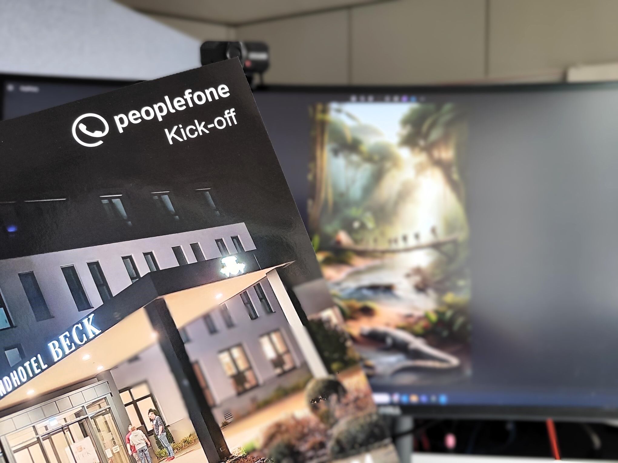 Vor einem Bildschirm wird ein Heft hochgehalten, mit Bildern von einer Veranstaltung.