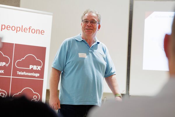 Eine Person steht vor einem Banner und hält einen Vortrag. Im Hintergrund ist eine Präsentation geöffnet.