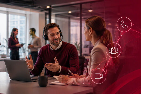 Zwei Personen im Büro sitzen am Schreibtisch und unterhalten sich. peoplefone MICROSOFT TEAMS.