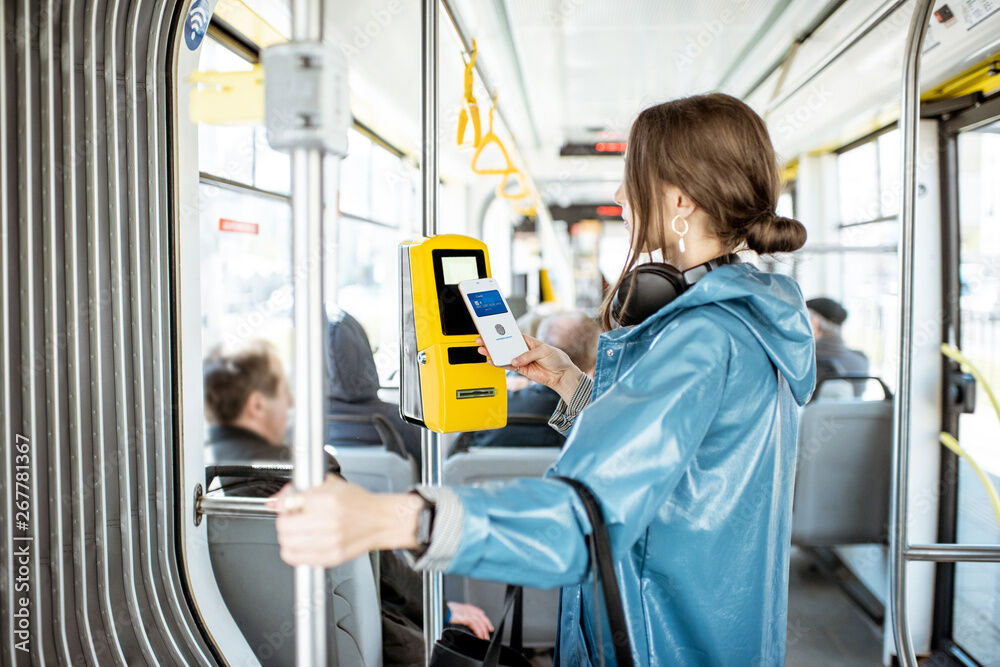 Eine Frau im blauen Regenmantel steht im Bus und hält ihr Handy an den Fahrkartenautomaten.