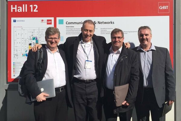 peoplefone Mitarbeiter vor einer Messewand der CeBIT schauen in die Kamera.