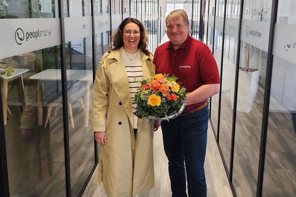 Zwei Personen stehen im Flur und übergeben einen Blumenstrauß