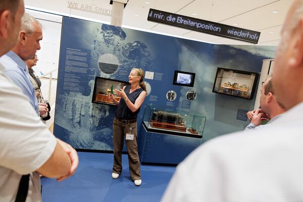 Mehrere Personen stehen in der Ausstellung und hören zu.