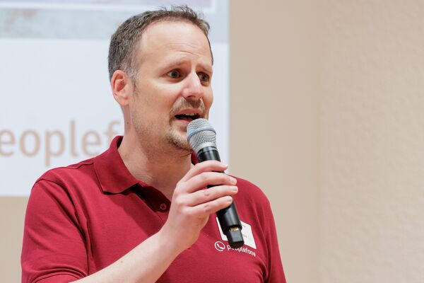 Jörg Hummer mit Mikrofon in der Hand begrüßt Gäste.