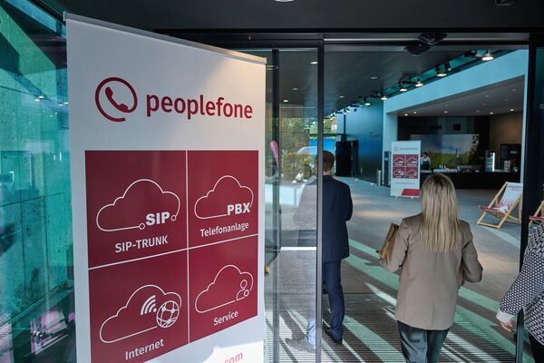 Personen gehen durch eine Glastüre. Auf der linken Seite steht ein peoplefone Banner.
