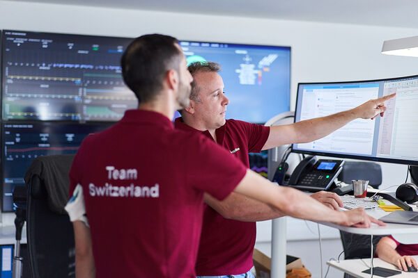 Zwei Personen im peoplefone Shirt stehen vor mehreren Bildschirmen und besprechen die Programmierung.