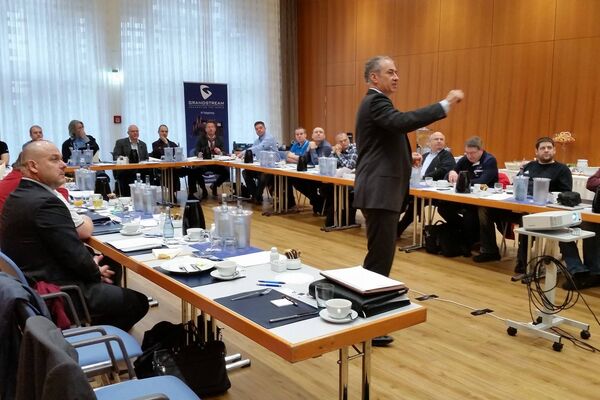 peoplefone Partner sitzend an Tischen in U-Form hören dem Referenten zu, der sich in der Mitte des Raums befindet.