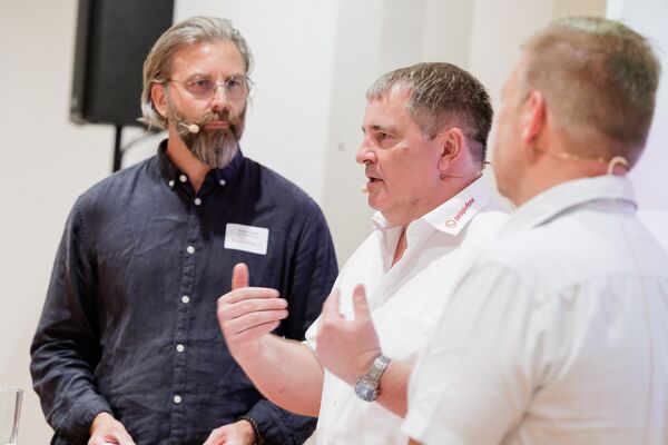 Drei Personen stehen vor einer Leinwand mit Headset und führen ein Gespräch.