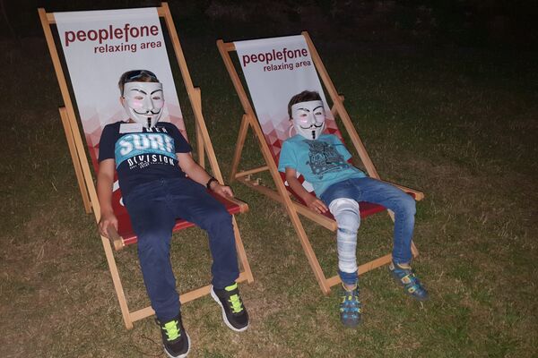 Zwei Kinder mit Masken liegen im Liegestuhl auf einer Wiese.