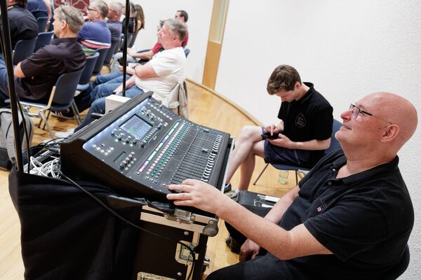 Techniker sitzt an einem Mischpult hinter dem Publikum bei einem Vortrag.