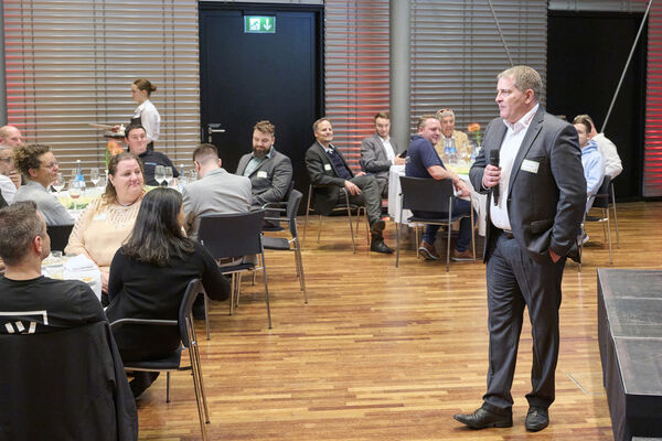 Geschäftsführer steht an der Bühne mit einem Mikrofon und spricht zu den Gästen.