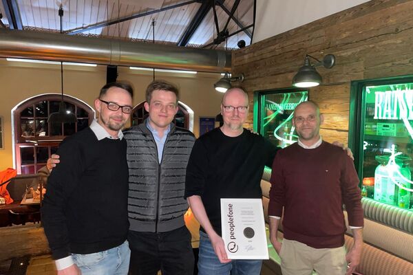 Vier Personen schauen in die Kamera und zeigen eine Urkunde in einem Lokal.