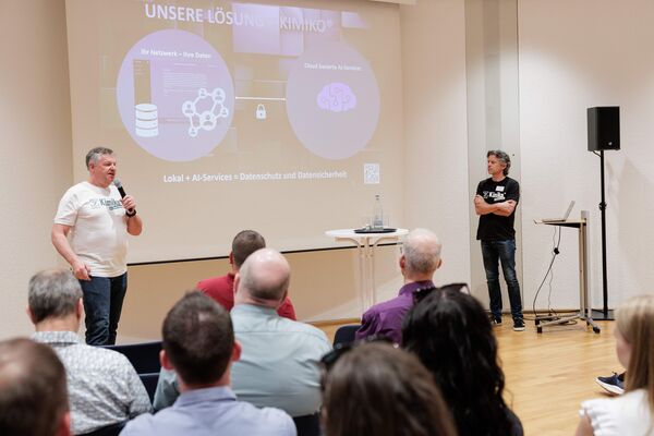 Zwei Personen stehen vor einer Leinwand und präsentieren.