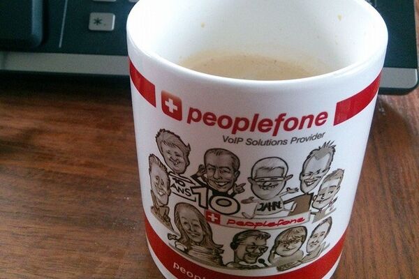 peoplefone Tasse steht vor einem Telefon.