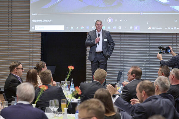 Geschäftsführer steht auf der Bühne und hält eine Ansprache mit einem Mikrofon in der Hand.