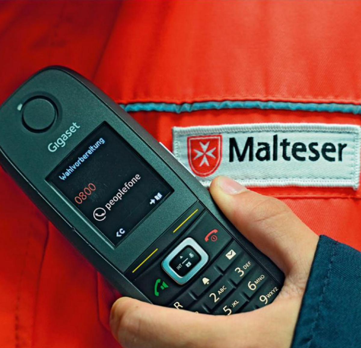 Mobiltelefon vor einer Weste der Malteser.