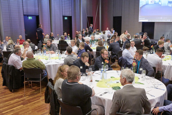 Personen sitzen im Raum an runden Tischen zusammen und reden.