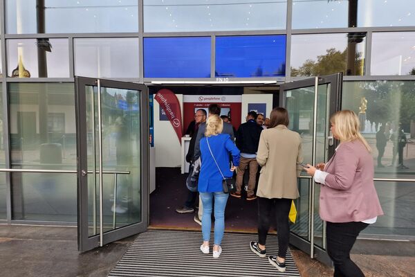 Mehrere Personen gehen durch einen Messeeingang auf einen Stand zu.