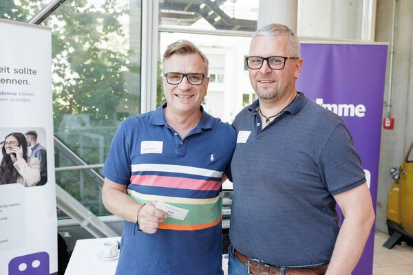 Zwei Personen zwischen Bannern schauen in die Kamera.