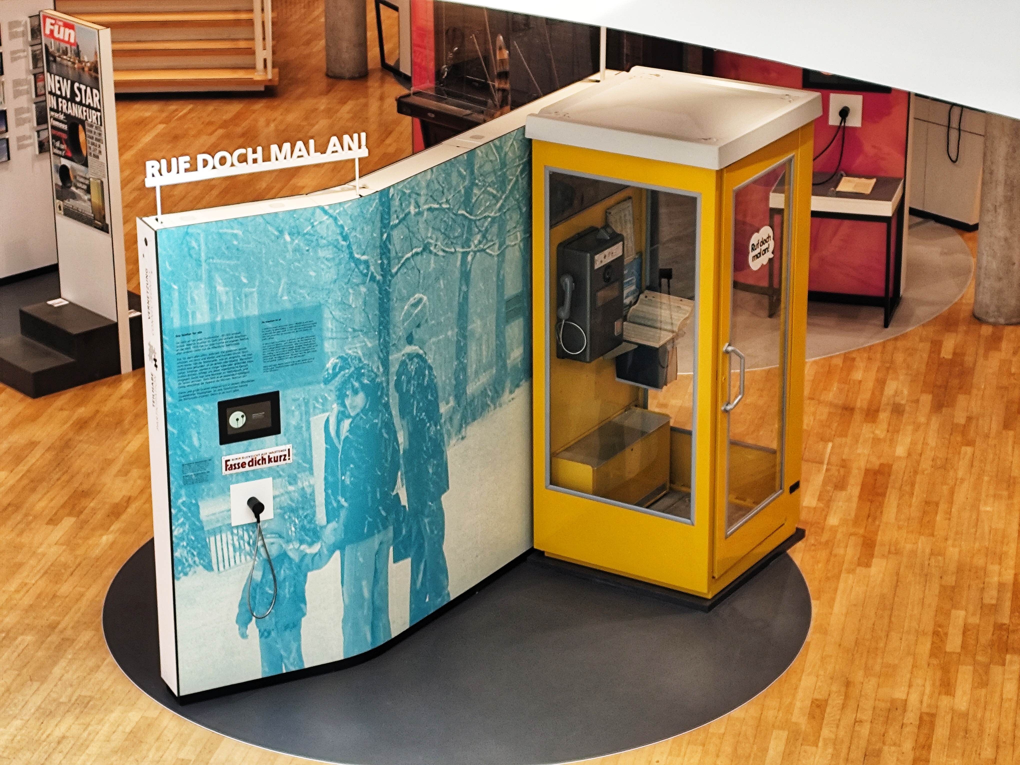 Ausstellungwand mit gelber Telefonzelle von oben.