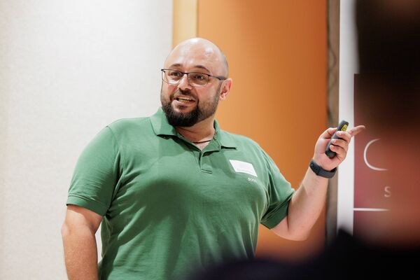 Eine Person steht vor einem Banner und hält einen Vortrag. Im Hintergrund ist eine Präsentation geöffnet.